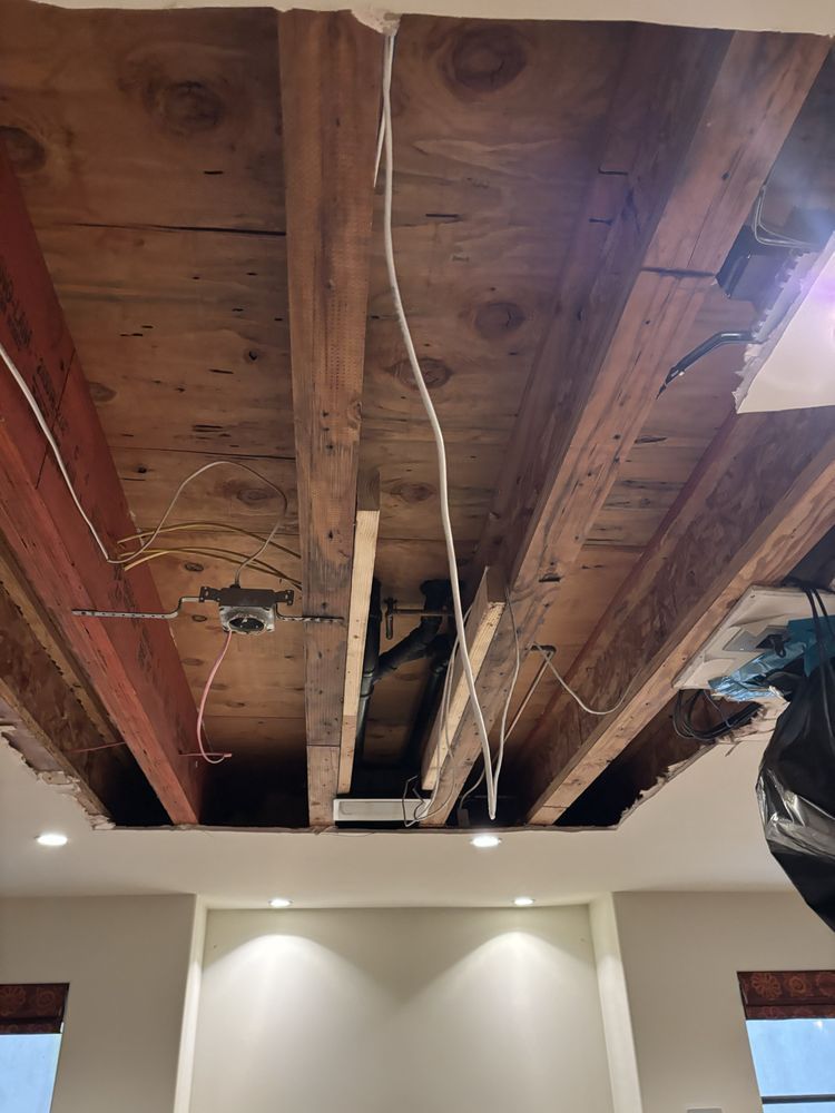 Exposed wooden ceiling with beams and wiring. Recessed lights illuminate the white walls below.