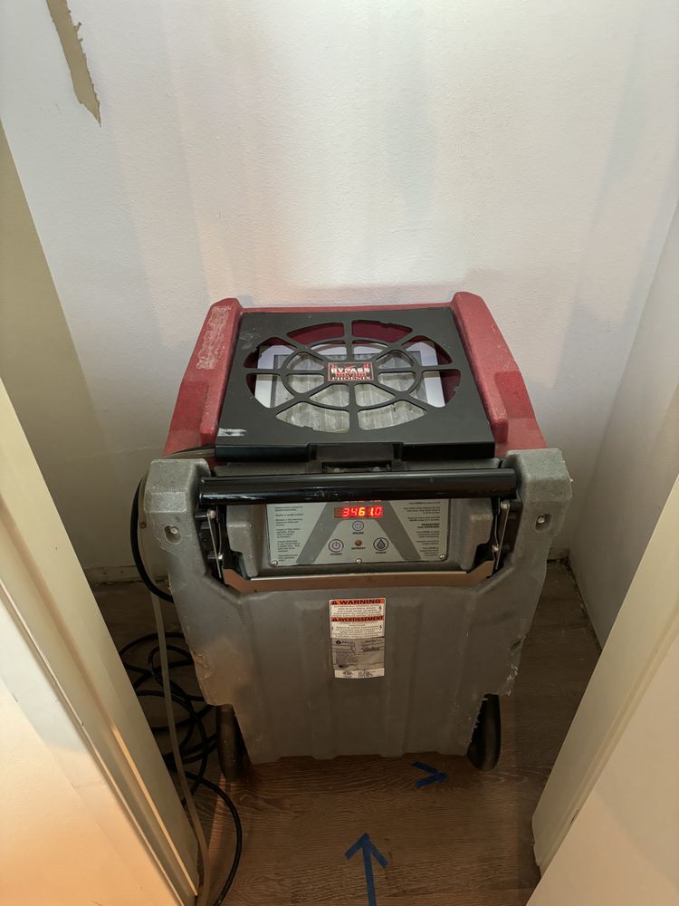 Dehumidifier in a closet, gray and red, with a digital display, on a wood floor. Blue arrow on the floor.