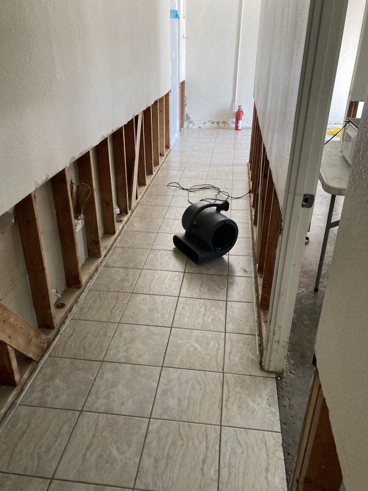 Hallway with exposed studs, floor tiles, and a black fan.