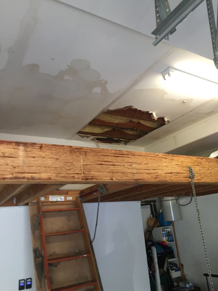 Water damaged garage ceiling with a hole and wooden beam, a ladder, and garage door hardware are visible.