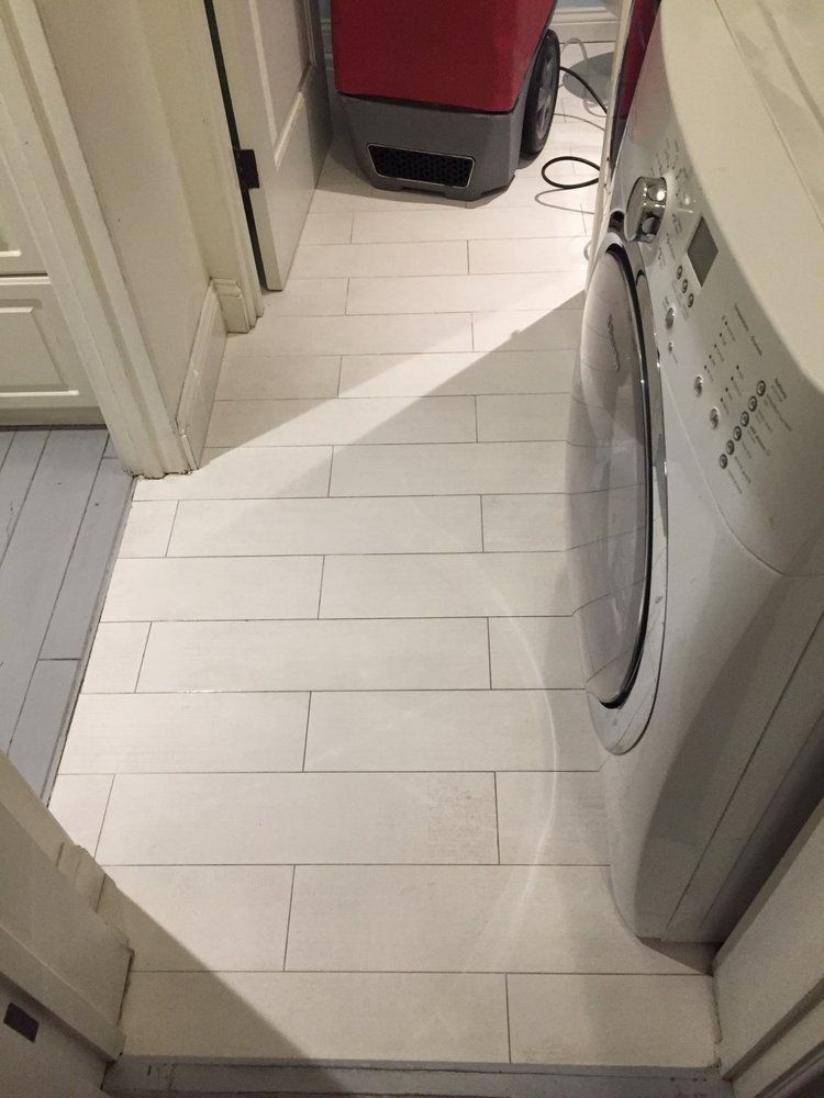 White-painted wood floor in a narrow hallway with a washing machine to the right and a door on the left.