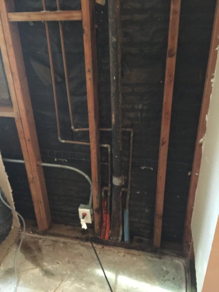 Framing of a wall with pipes and electrical wiring visible.