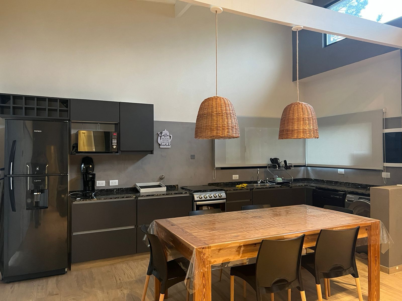 Cocina moderna oscura con armarios grises, electrodomésticos y una mesa de madera con sillas negras.