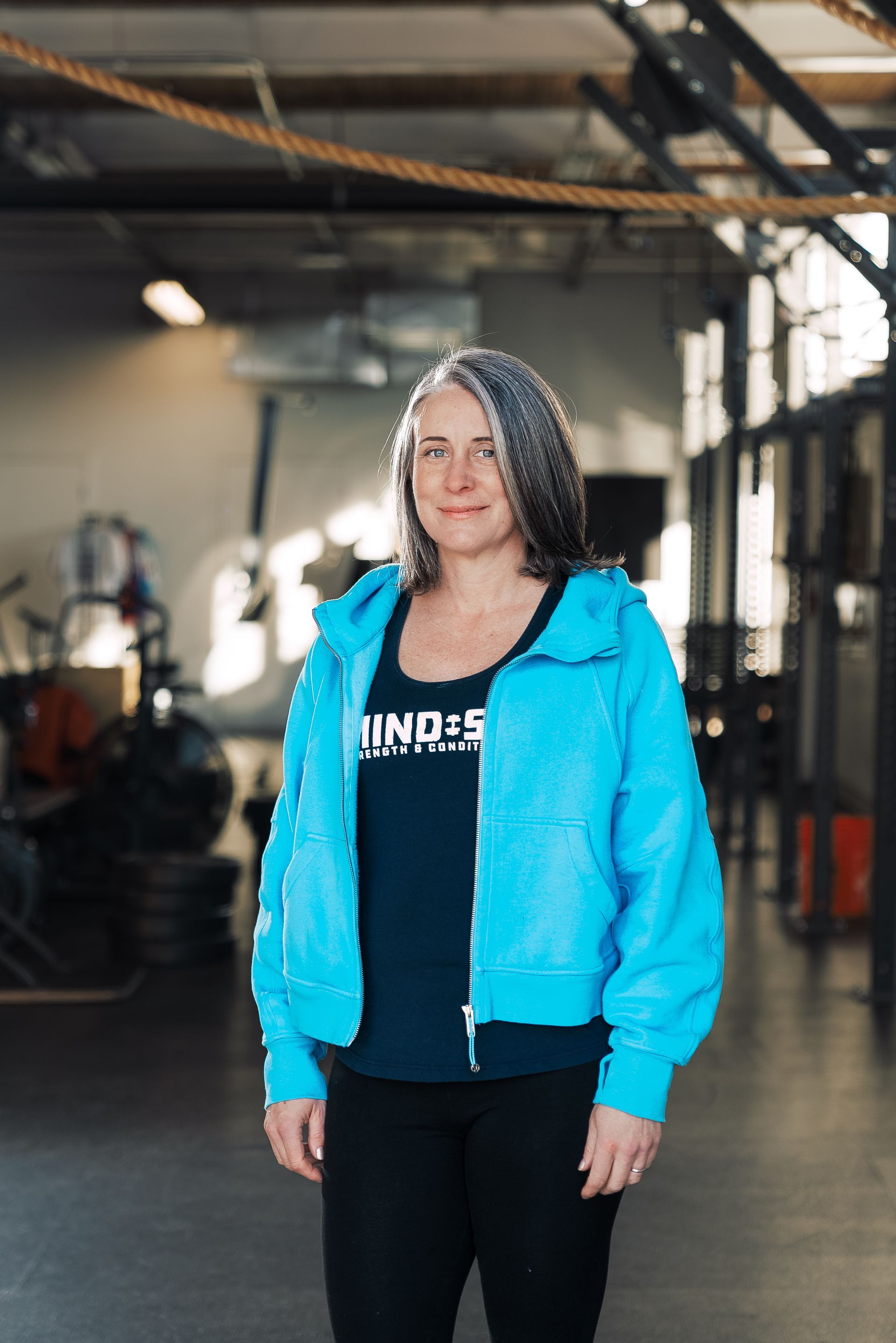 A woman in a blue jacket is standing in a gym.