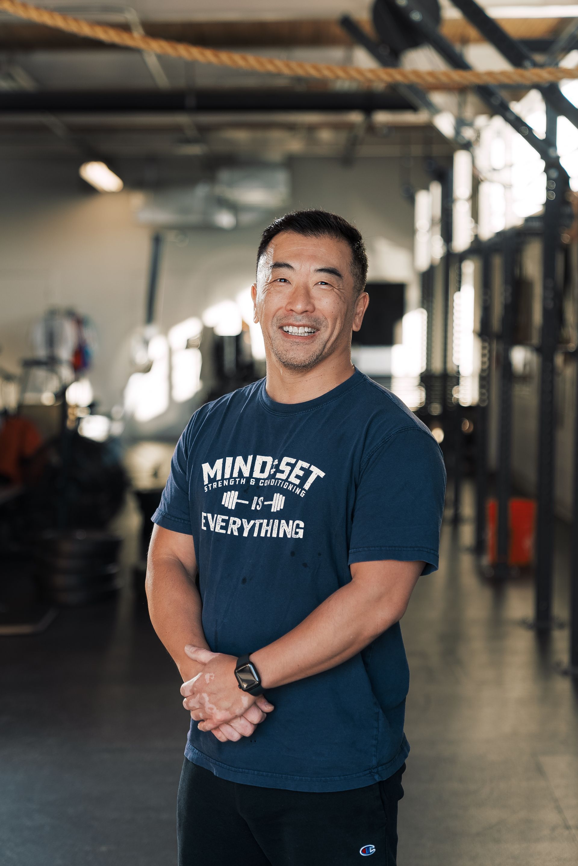 A man in a blue shirt is standing in a gym with his hands folded.