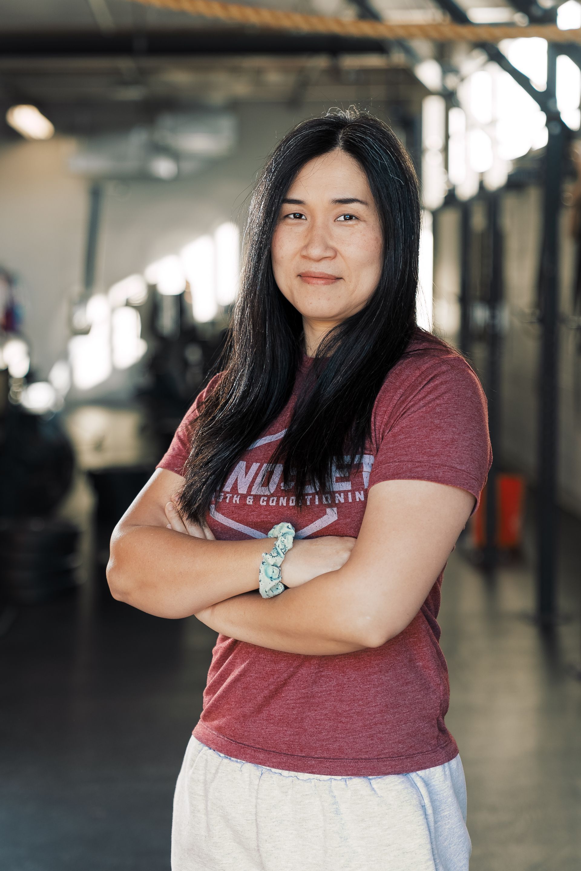 A woman is standing in a gym with her arms crossed.