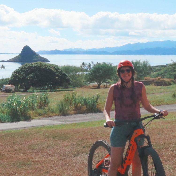 A woman wearing a red helmet stands next to an orange bike