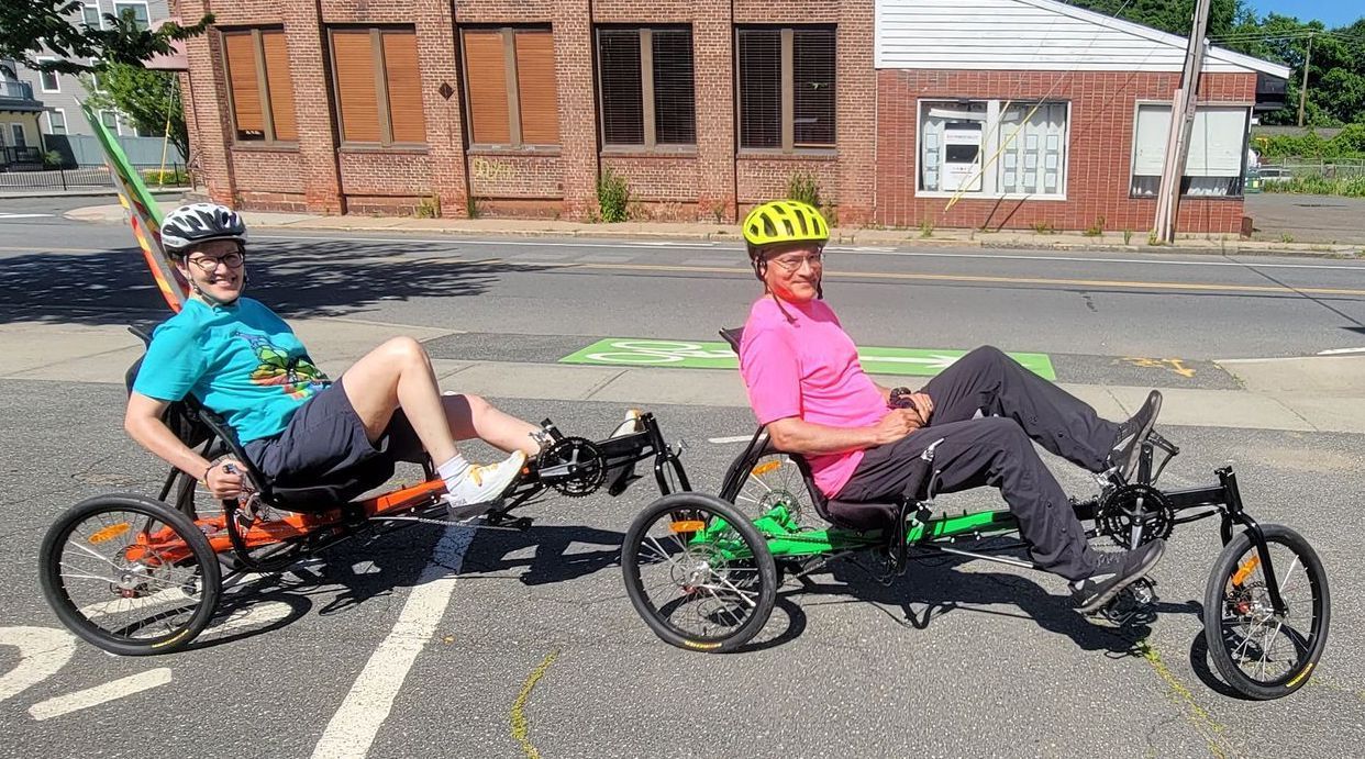 Two people wearing helmets are smiling while riding recumbent bicycles in Northampton, MA