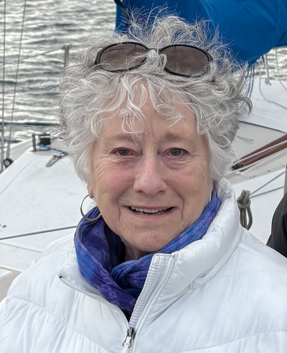 Image shows a woman with a white jacket, smiling at the camera while sunglasses rest on her head.