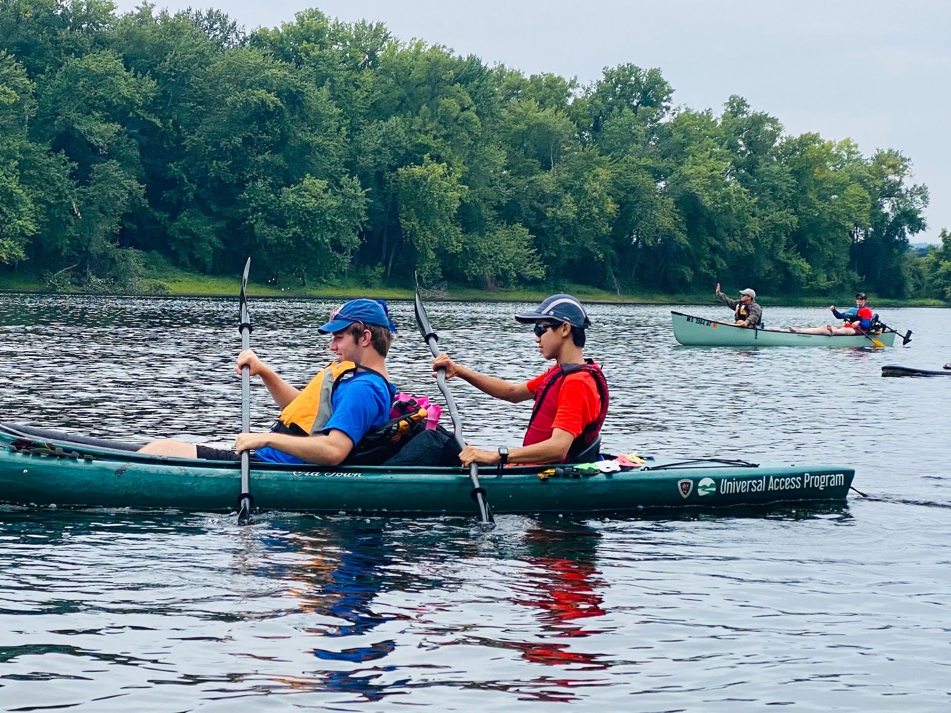2 people in the foreground paddle in a green tandem kayak; a canoe is behind them