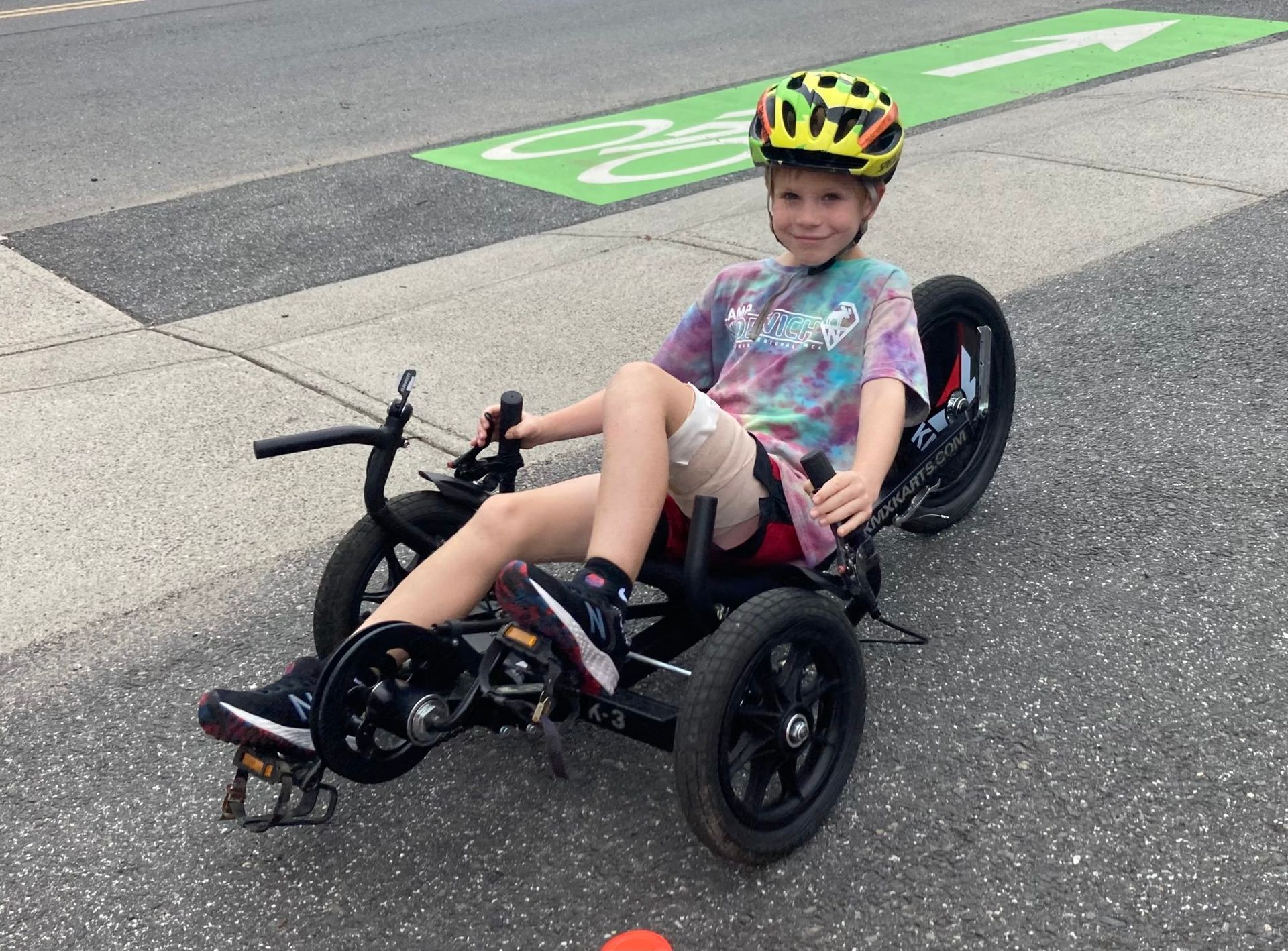 A young boy wearing a helmet is riding a KMX K-3 recumbent trike.