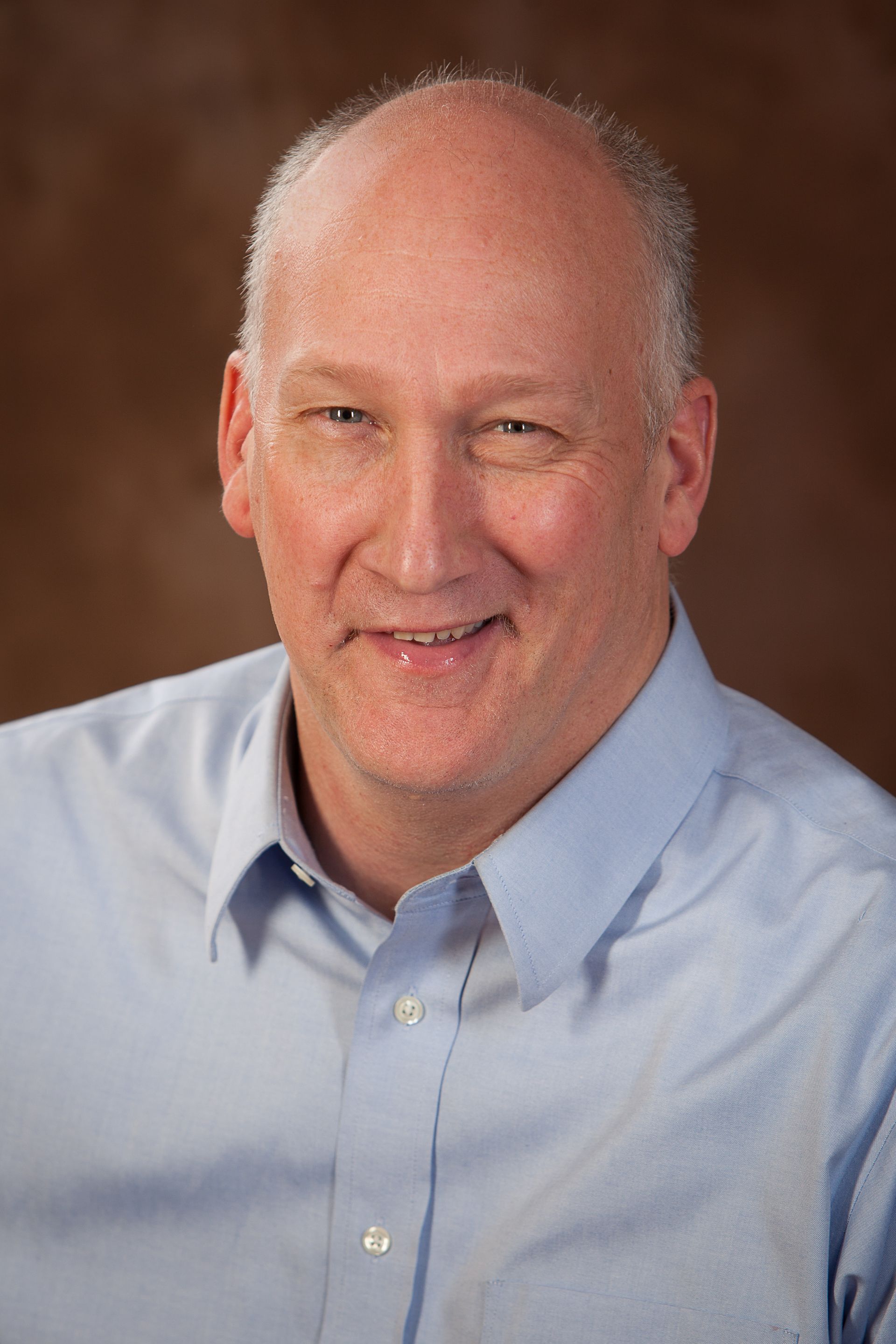 Image is of a man in a button up shirt smiling at the camera