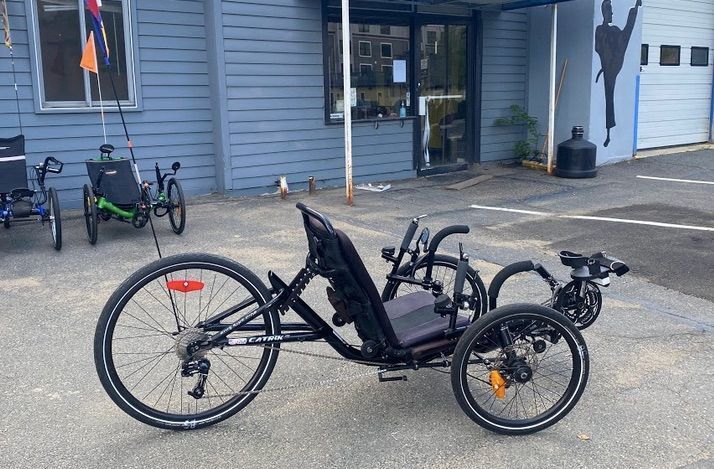 A black Catrike 5.5.9 recumbent tricycle is parked in front of a building.