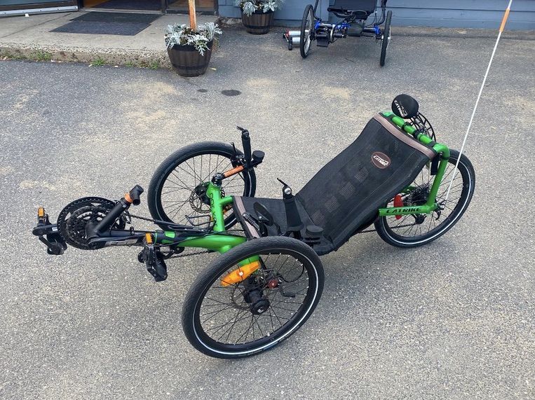 A compact, green recumbent tricycle with a low seat and head rest is parked in a parking lot.