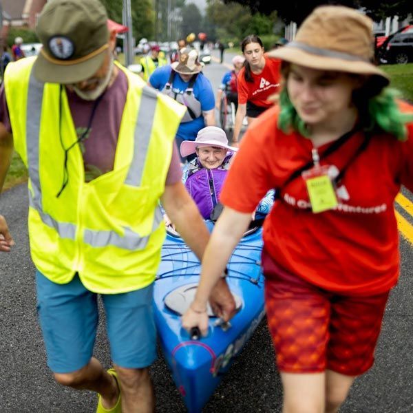 Several people ferry a woman in a kayak to the water's edge.