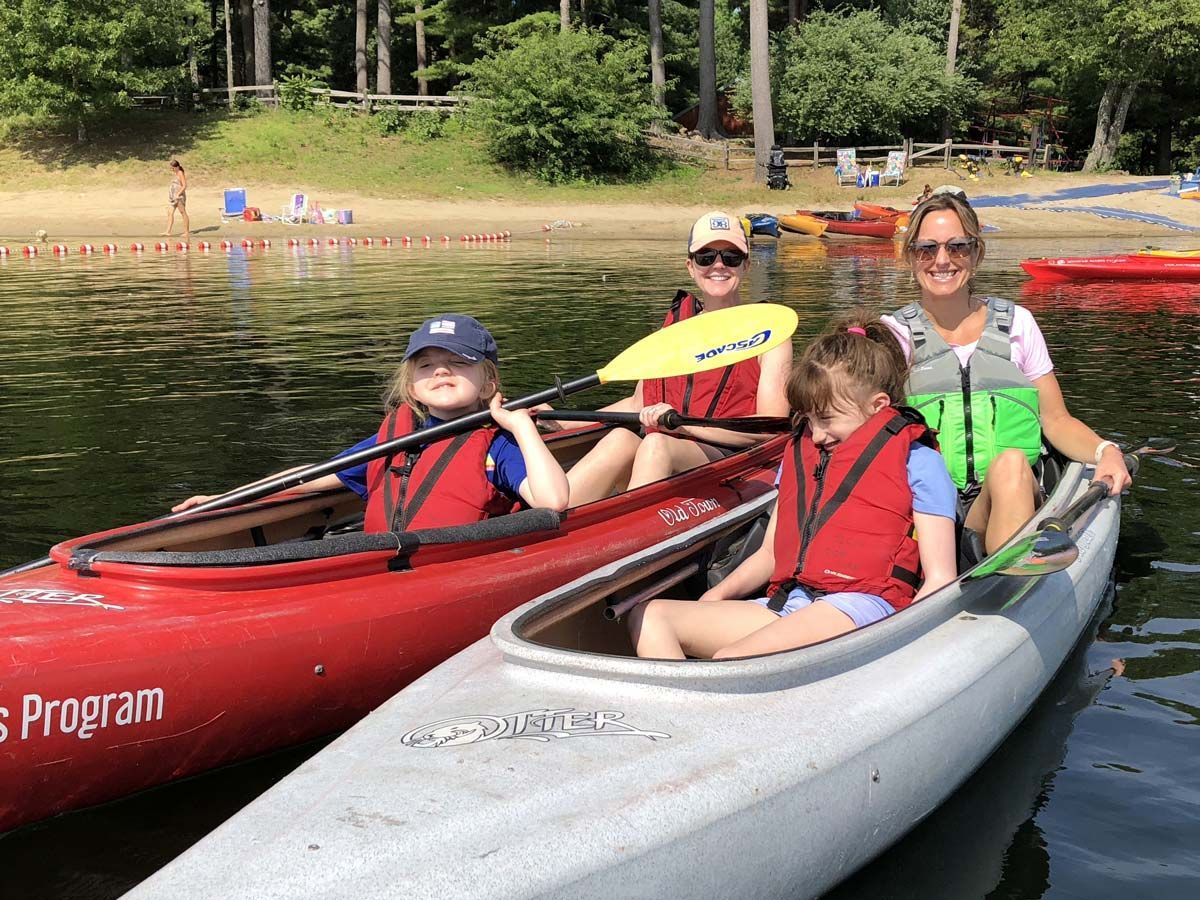 Two adults and two children sitting in kayaks on a lake, smiling at the camera.