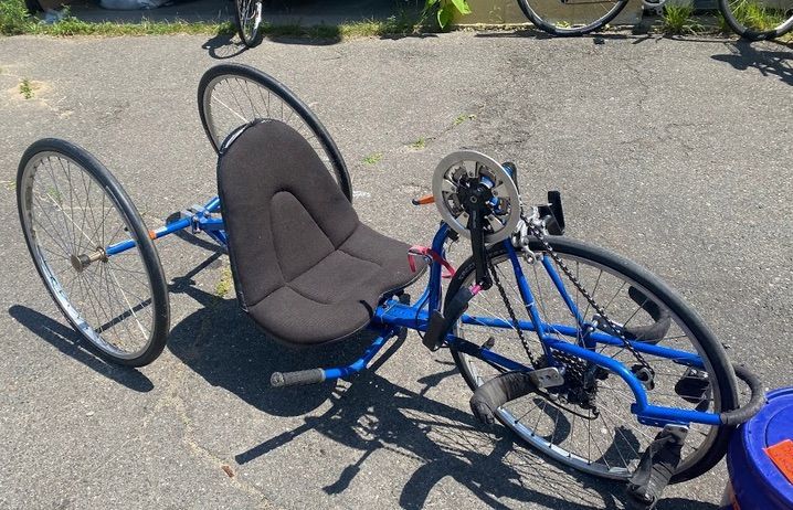 A blue Freedom Ryder handcycle (hand-powered tricycle) with a low-to-the-ground padded seat.