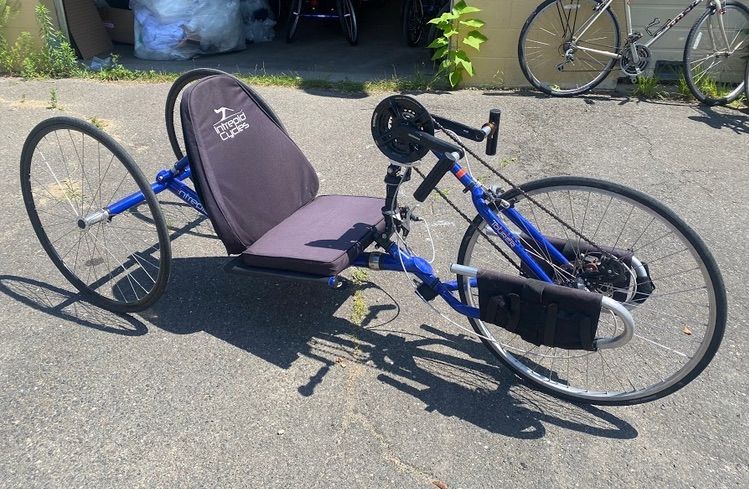 A blue Intrepid Tourer handcycle (hand-powered tricycle) with a low-to-the-ground, padded seat.