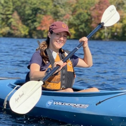 Kailean Hubbard smiles at the camera while rowing a kayak.