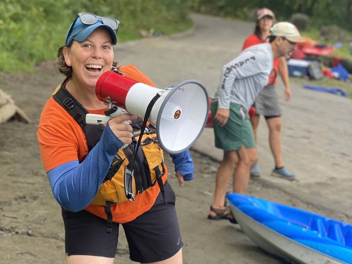 An All Out Adventures program leader smiles enthusiastically and talks into a bullhorn on a beach.