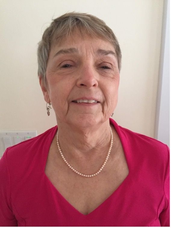 Leslie Stein, in a pink shirt, earrings, and pearl necklace, smiles at the camera.