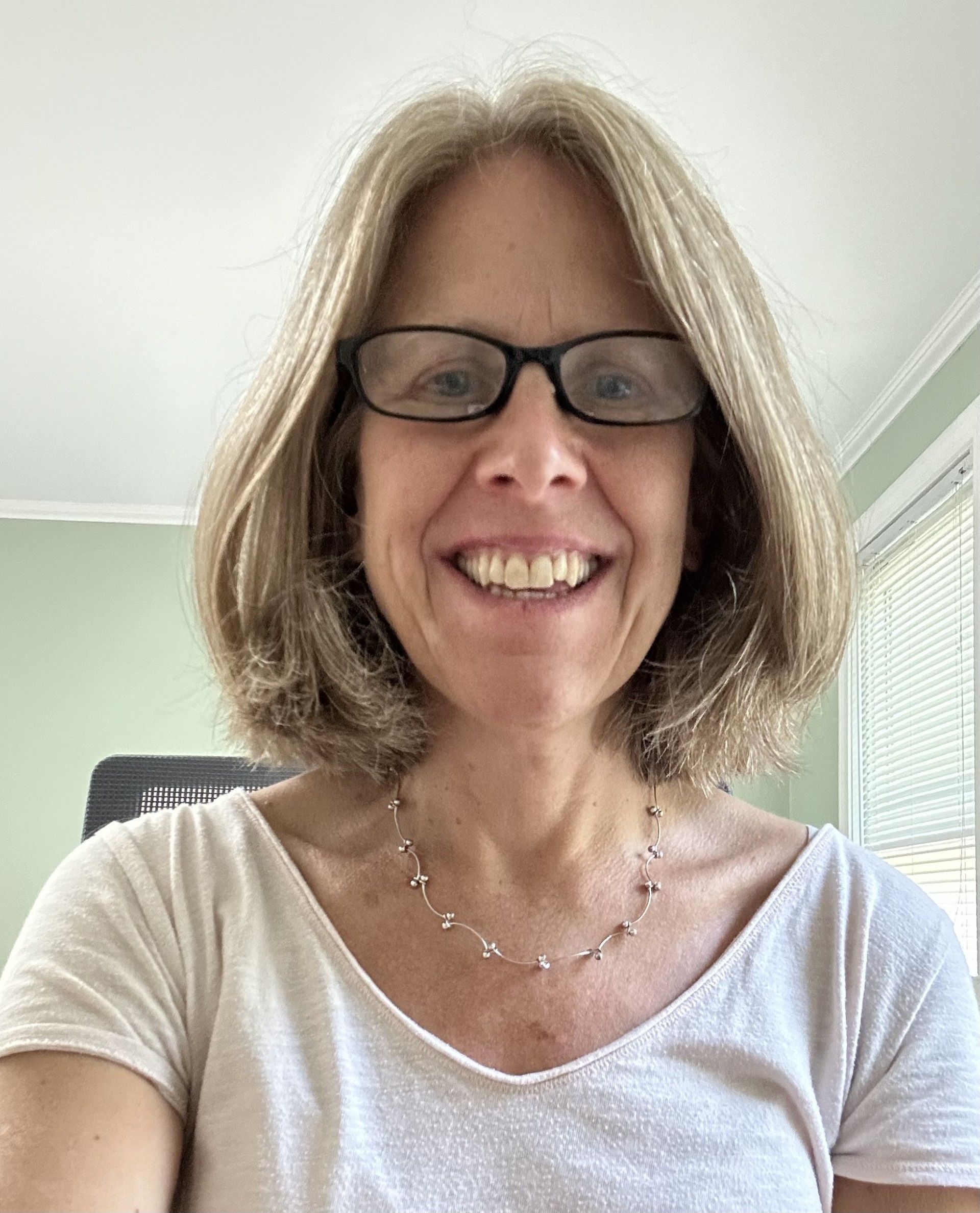 Image is of a woman with shoulder length brown hair, glasses, and a friendly smile