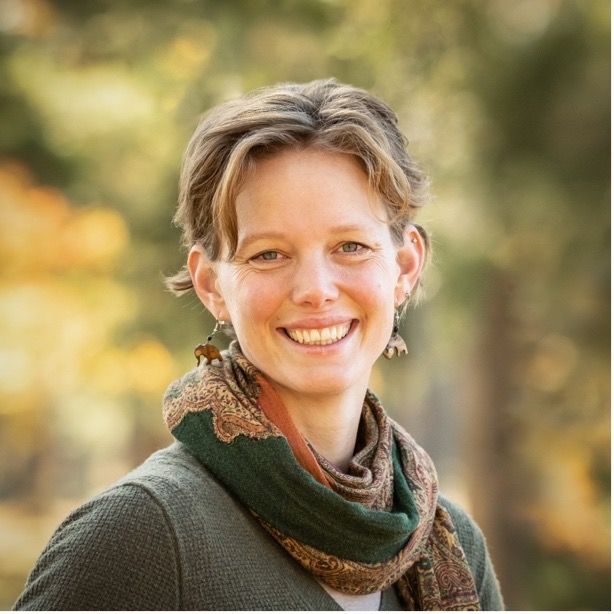 Liz Martin, wearing a scarf and earrings, smiles at the camera in an outdoor setting.