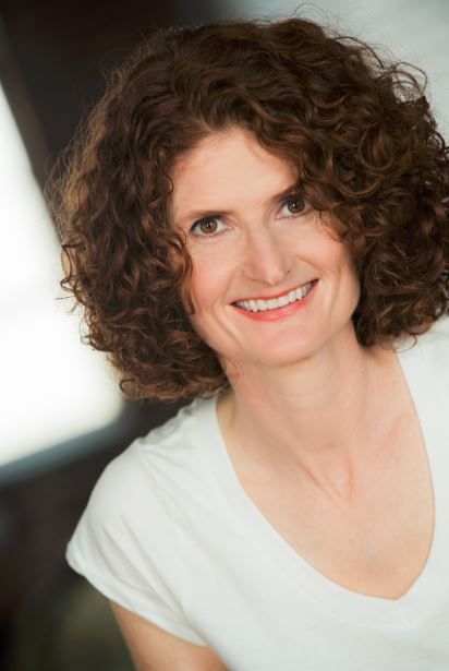 Susan Tracy, with curly hair and a white shirt, smiles at the camera.