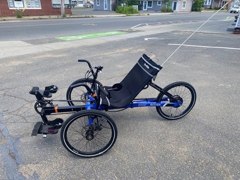A blue recumbent TerraTrike Rover tricycle with assist arms is parked in a parking lot.