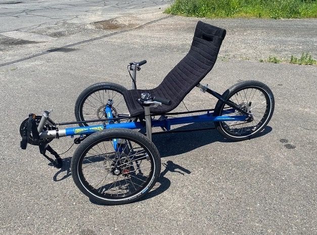 A blue recumbent Trident Trikes recumbent trike is parked on the side of the road.