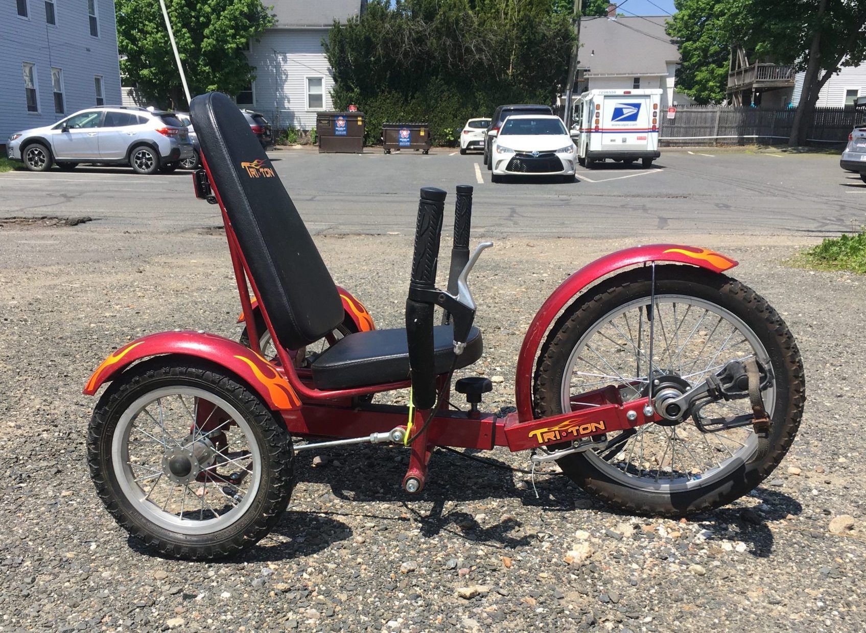 A small, upright kids trike in red with a flame motif and fat tires is parked in a parking lot.
