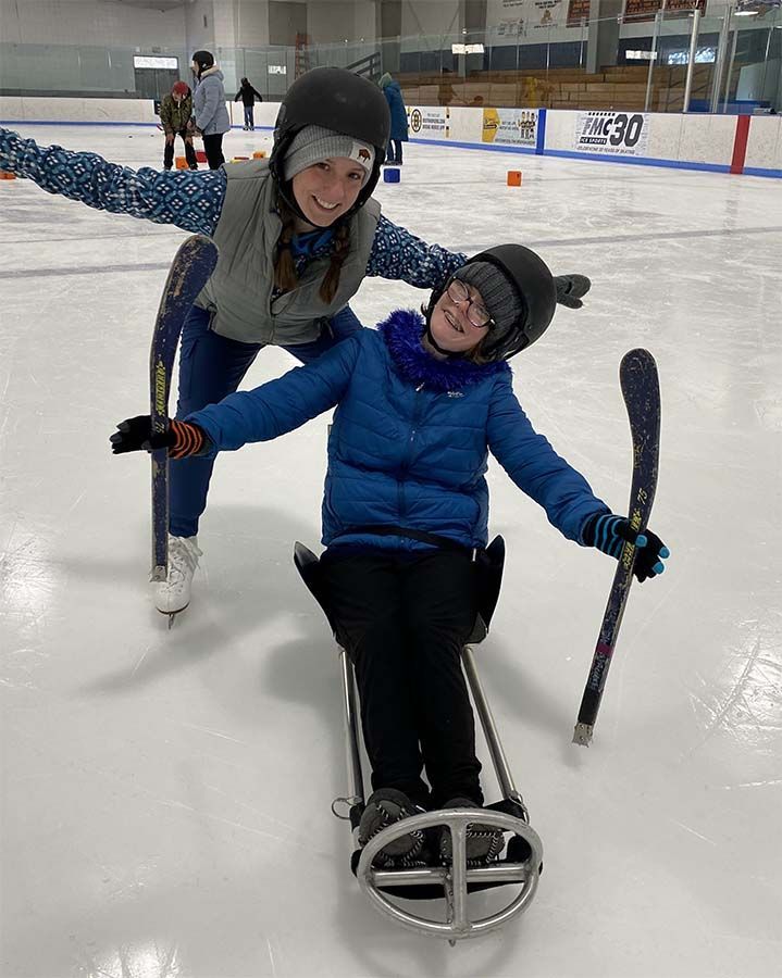 A young woman and  child grin and pose on ice skates and an ice sled.