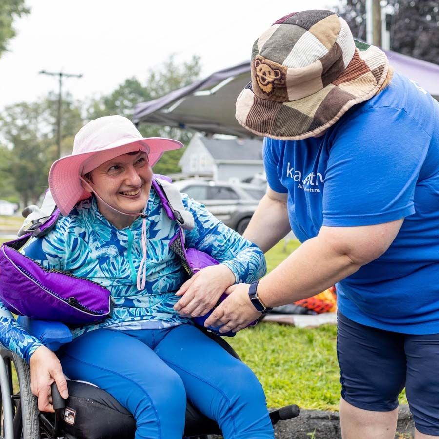 A program volunteer helps adjust the lifejacket of a woman in a wheelchair, who is smiling.
