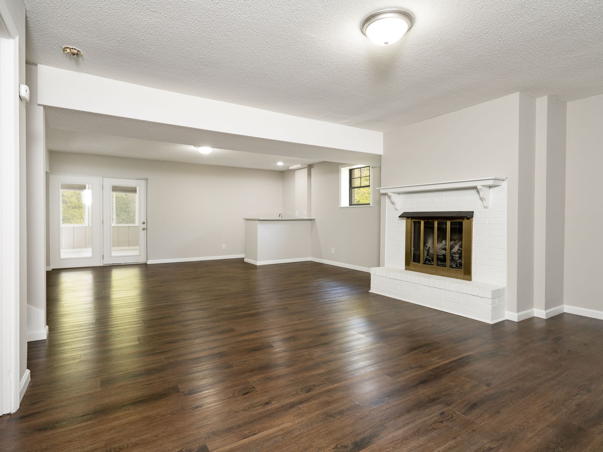 Empty living room with fireplace, wood floors, and French doors.
