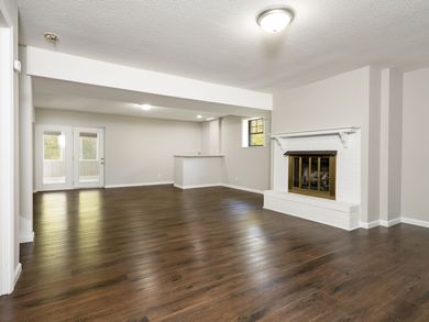 Empty living room with fireplace, wood floors, and French doors.