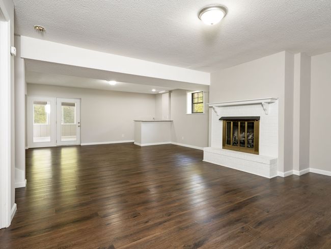 Empty living room with fireplace, wood floors, and French doors.