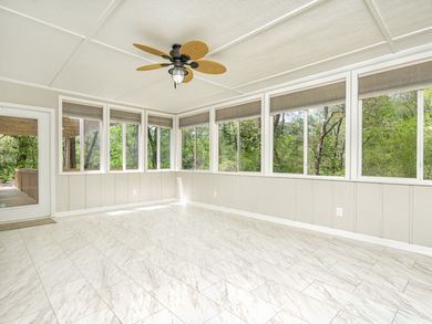 Sunroom with white walls, large windows overlooking trees, and tiled floor.