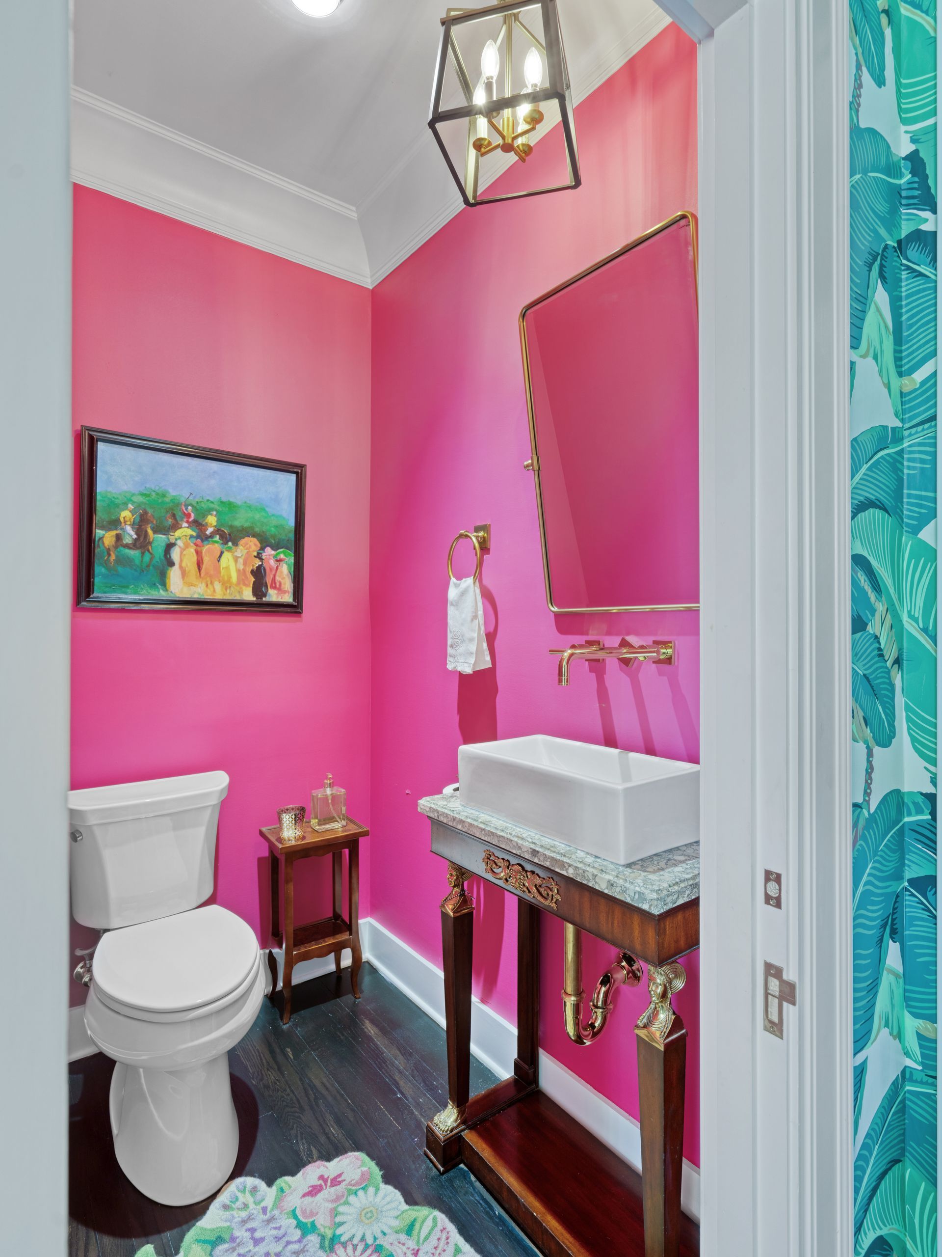 Bright pink powder room with white fixtures, brass accents, and a small decorative table.