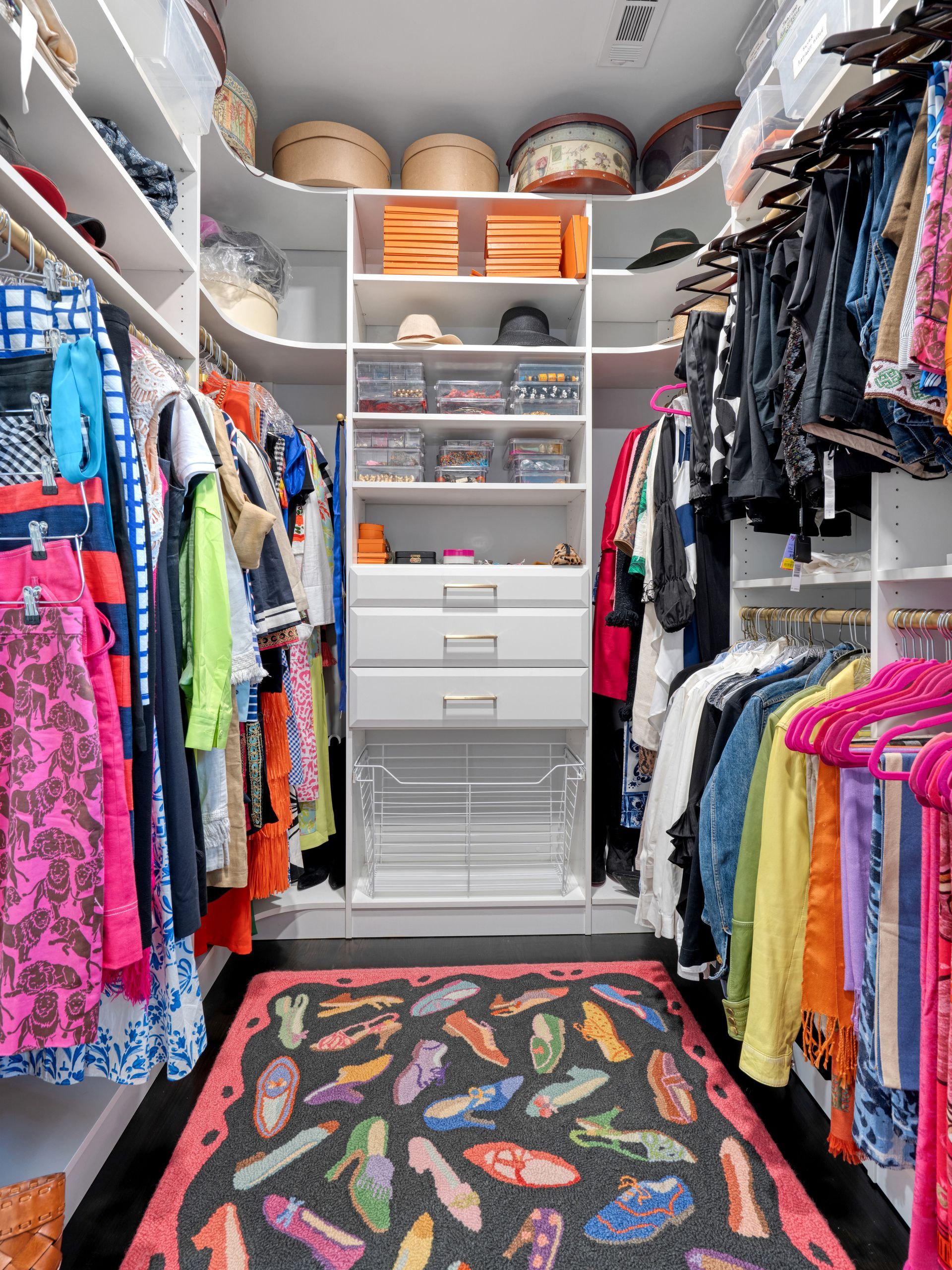 Walk-in closet with white shelves, clothing, and shoe-patterned rug.