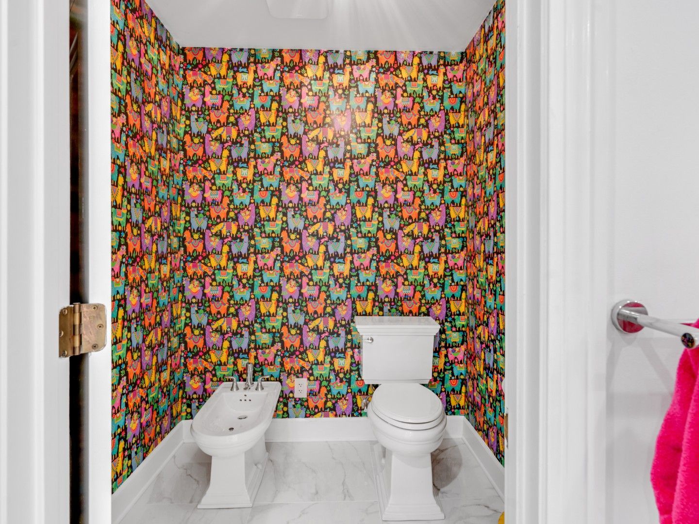 Small bathroom with colorful llama wallpaper, white toilet and bidet, seen from the doorway.