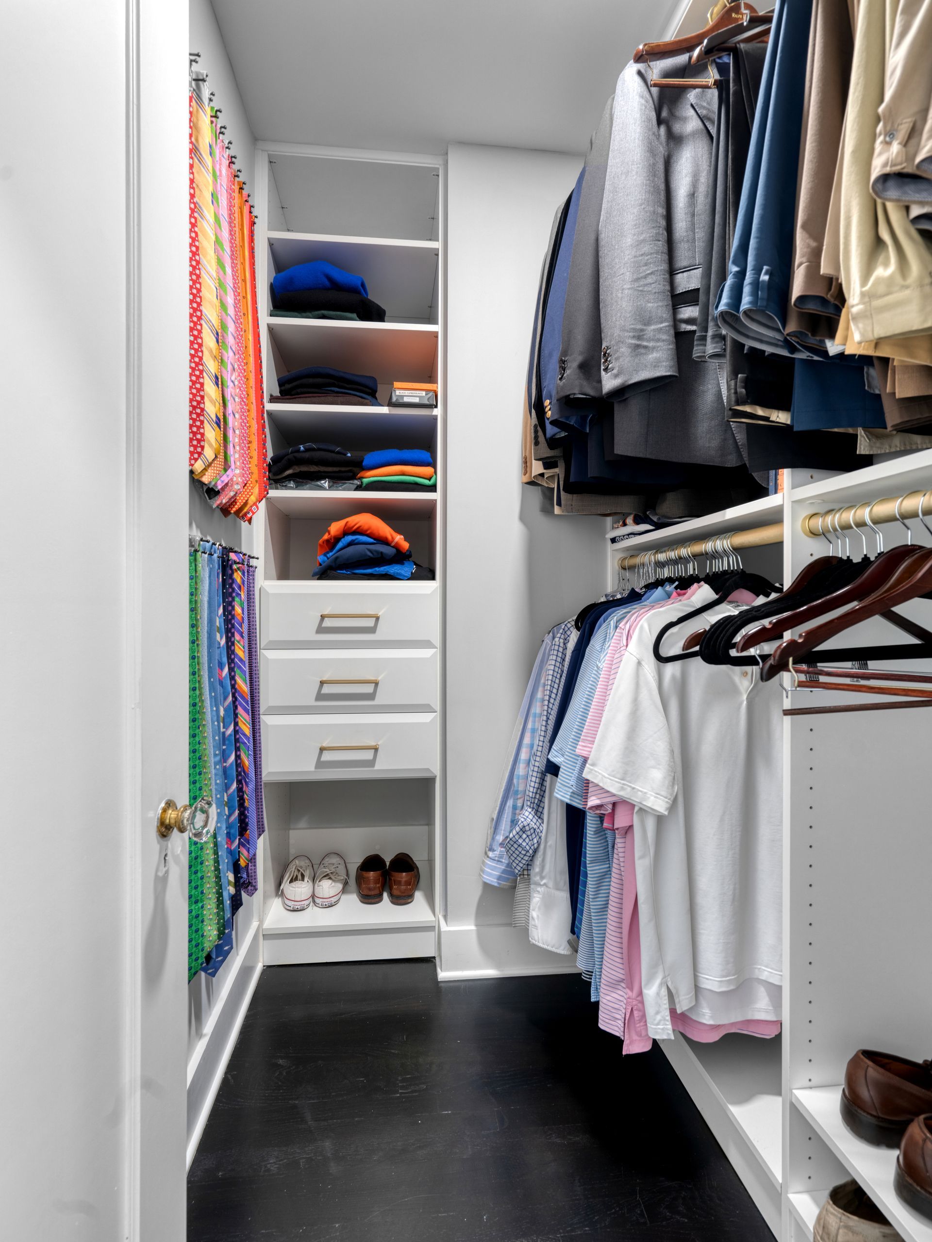 Walk-in closet with hanging clothes, shelves for folded items, and shoe storage. White shelves with black floor.
