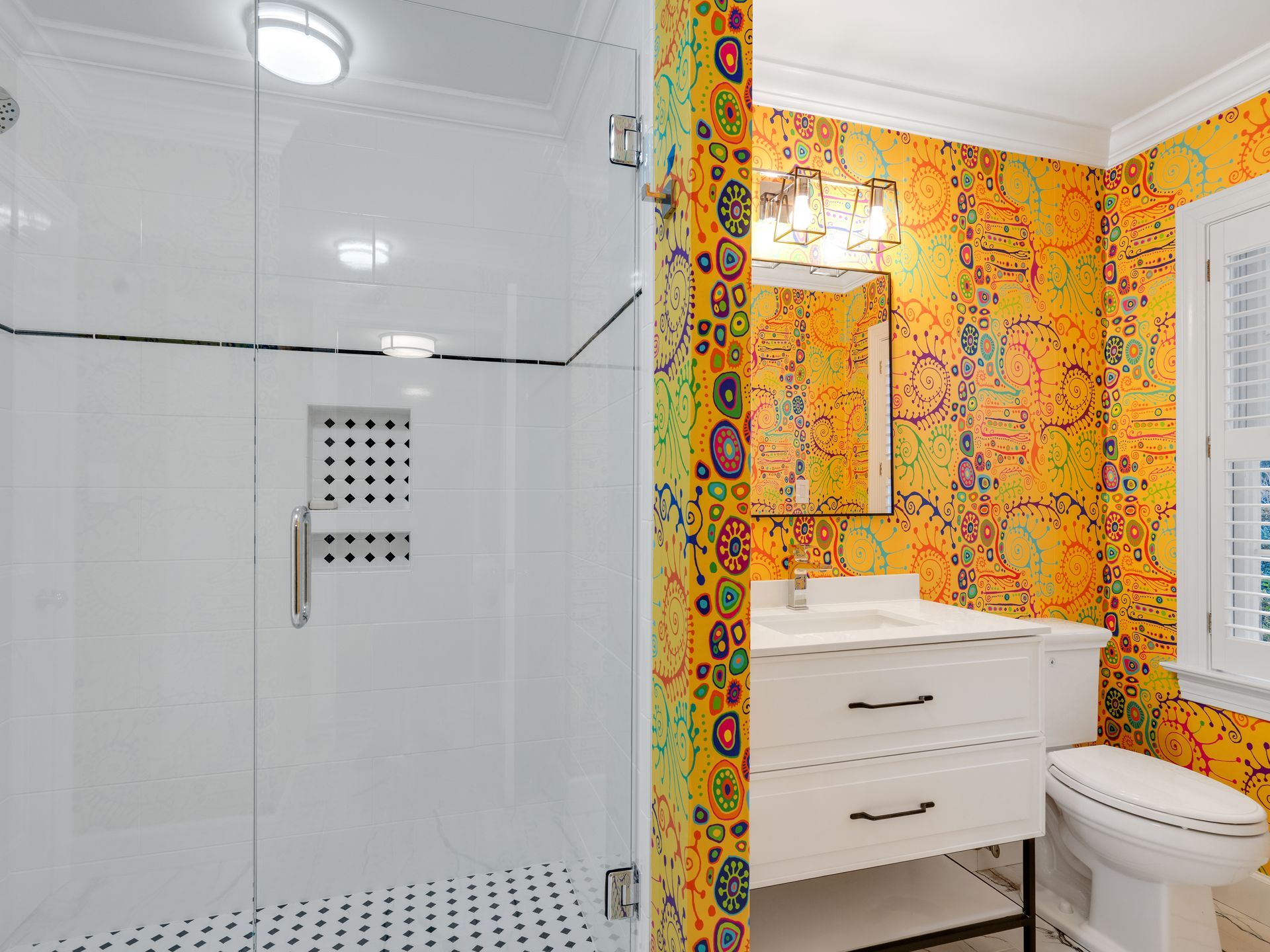 Bathroom with walk-in shower, white vanity, and brightly patterned wallpaper in yellow, green, and red.
