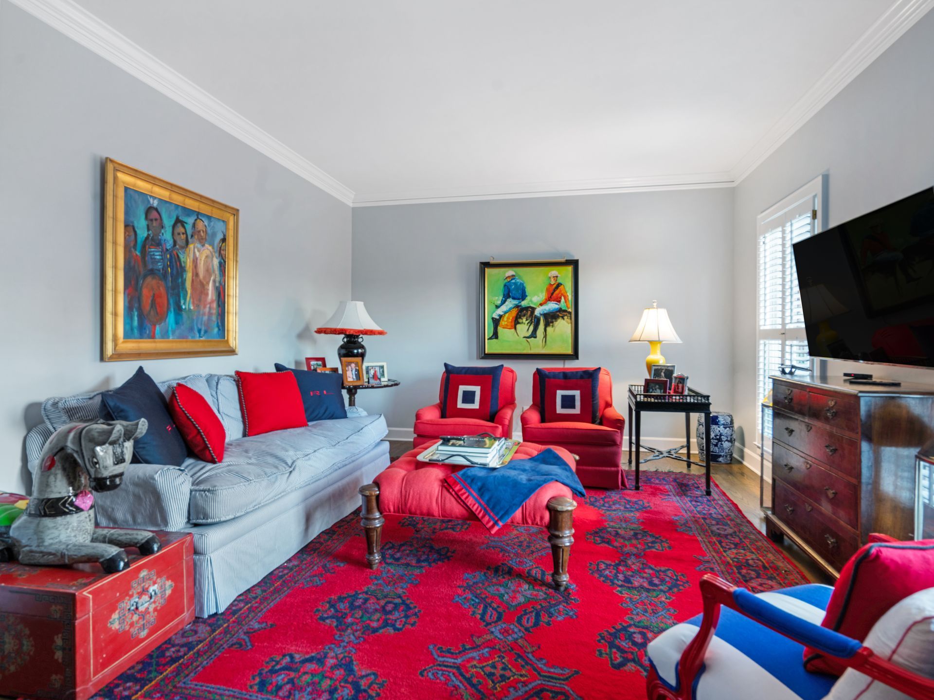 Living room with gray walls, red rug, sofa, chairs, artwork, and TV.