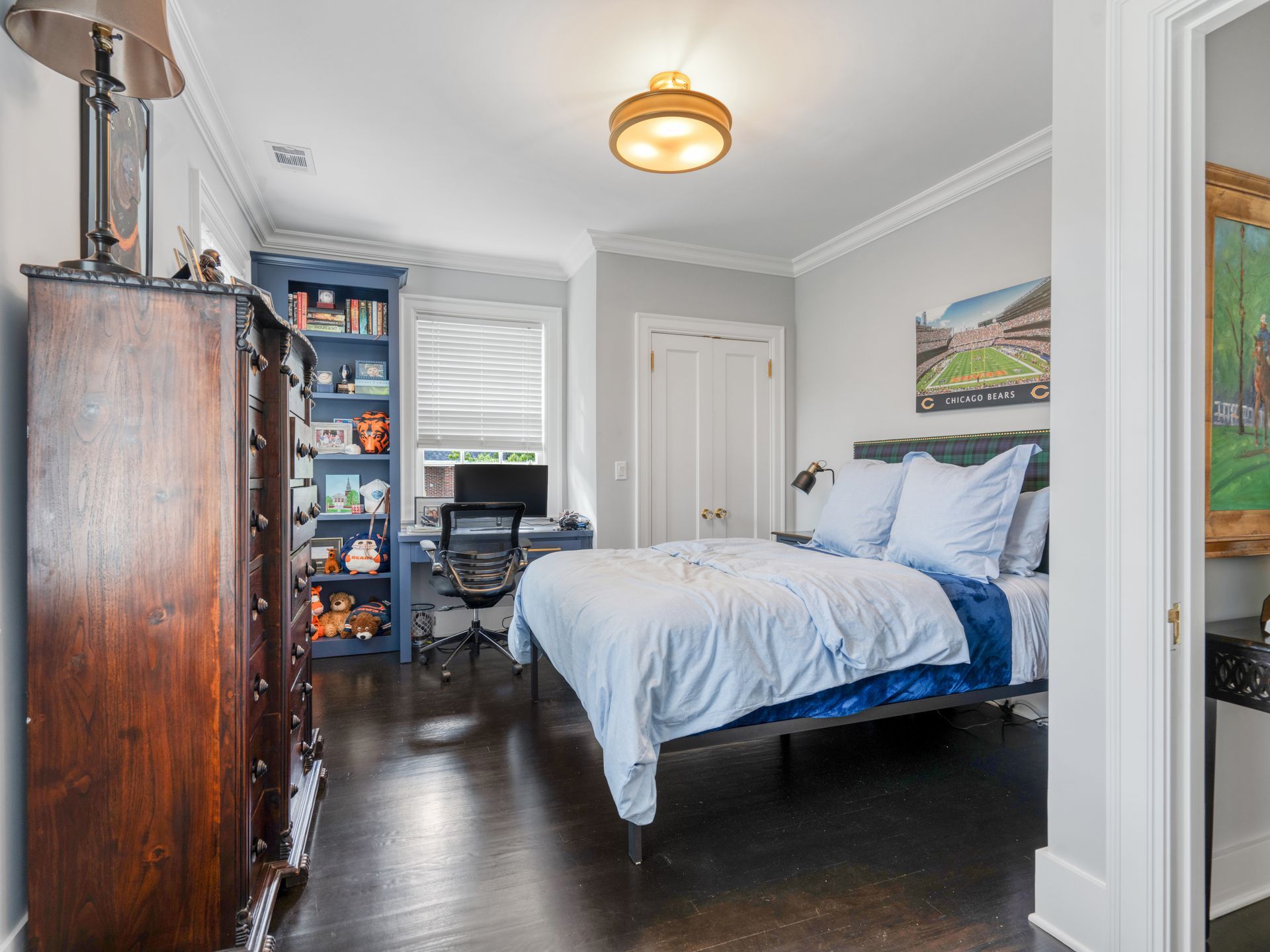 Bedroom with dark wood floors, bed, desk, built-in bookshelf, and chest of drawers.