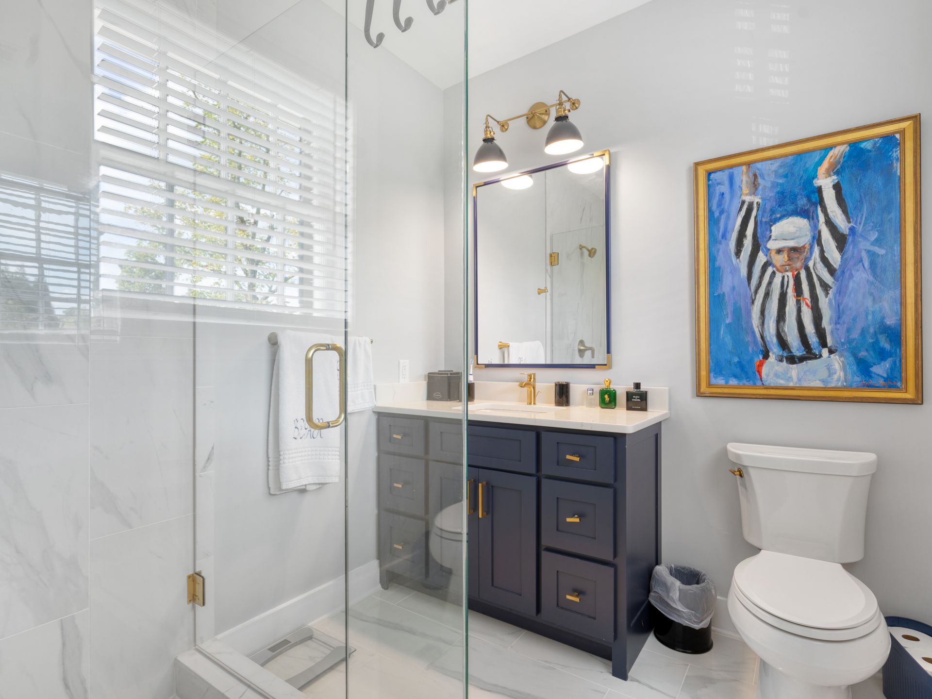 Bathroom with blue vanity, white toilet, and shower. Artwork of a referee hangs on the wall.