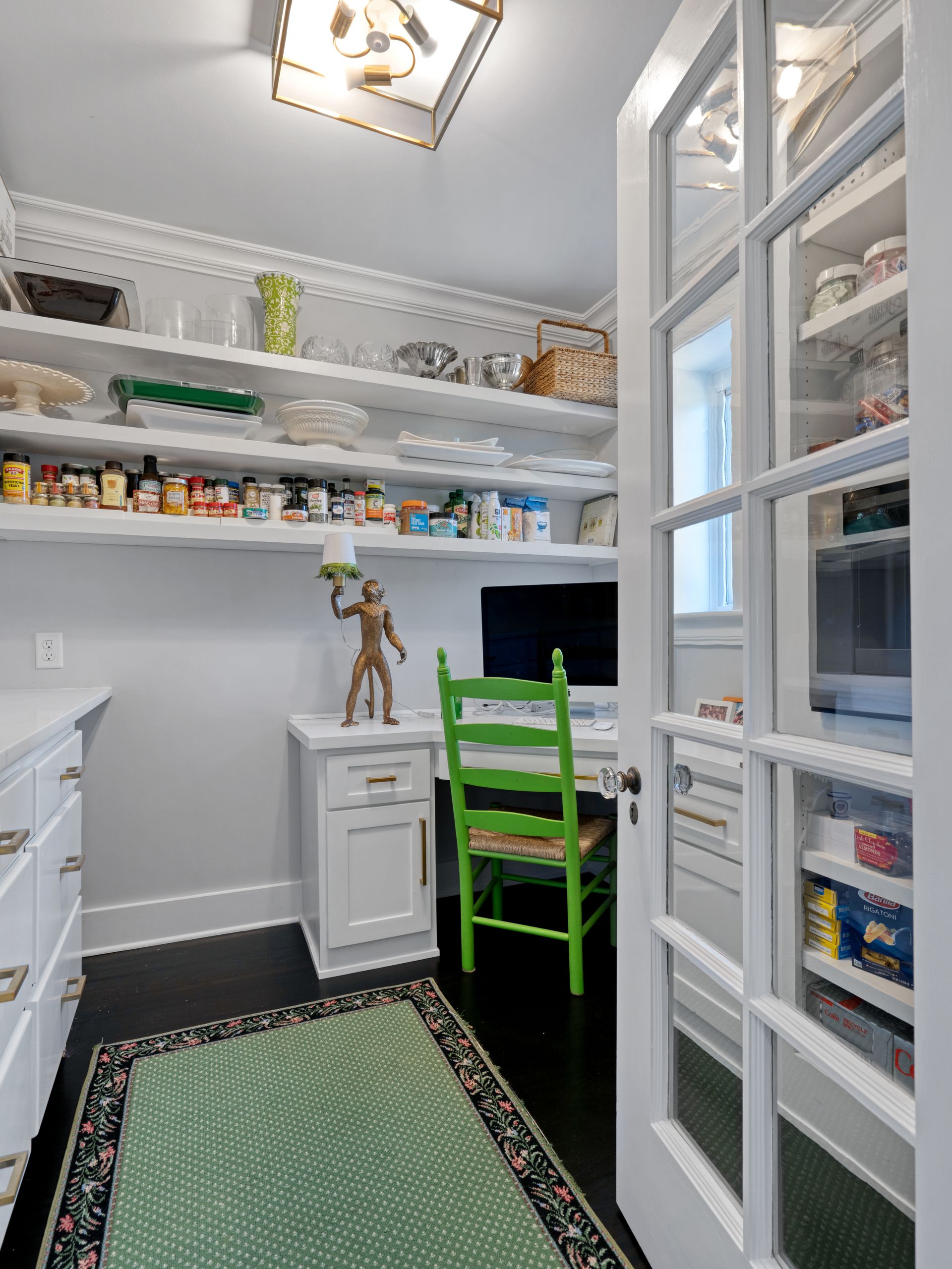 Pantry with white shelves and cabinets, a green chair, and a rug. Open door with food shelves.