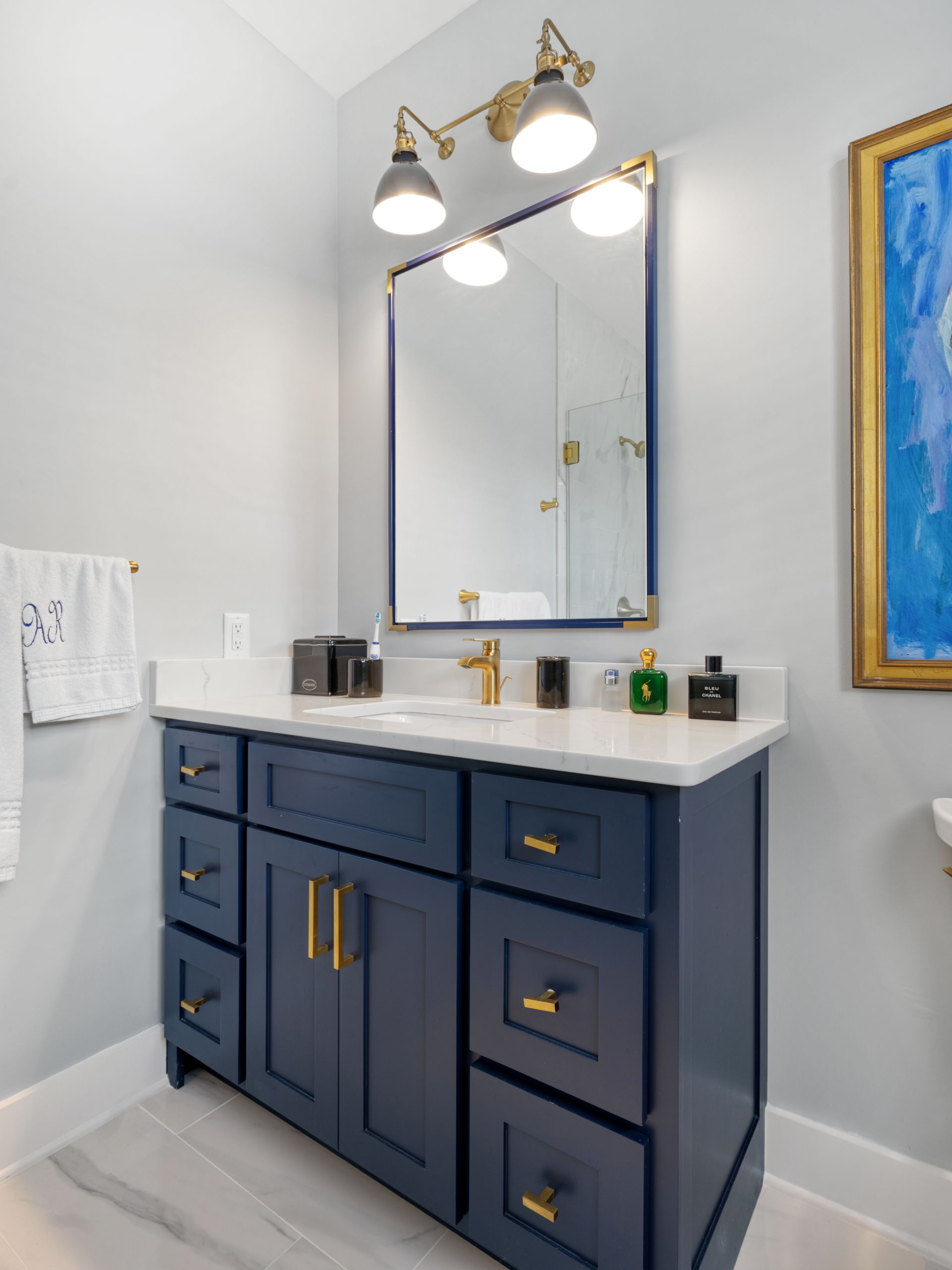 Navy blue bathroom vanity with gold hardware, white countertop, and mirror.