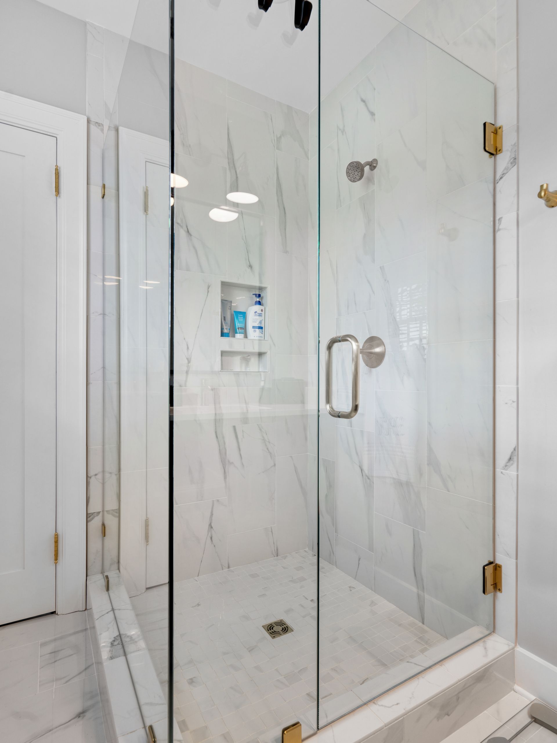 Glass-enclosed shower with white marble walls and gold hardware.