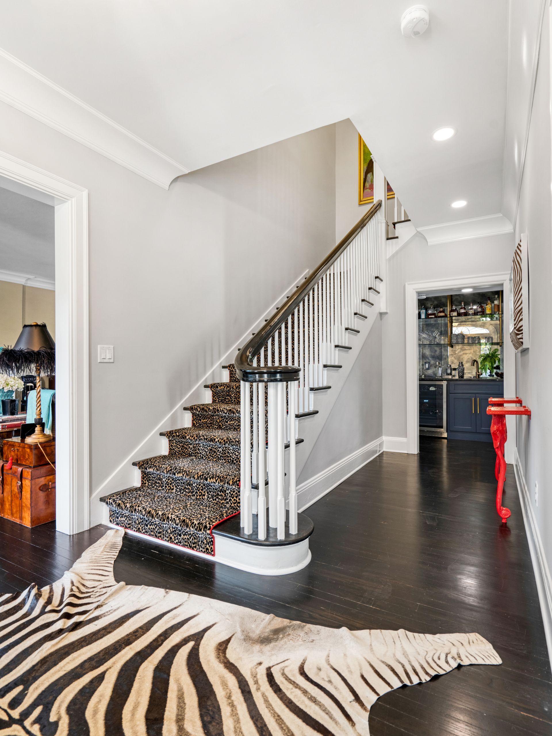 Hallway with black floor, staircase with patterned runner, zebra rug, and a small bar.