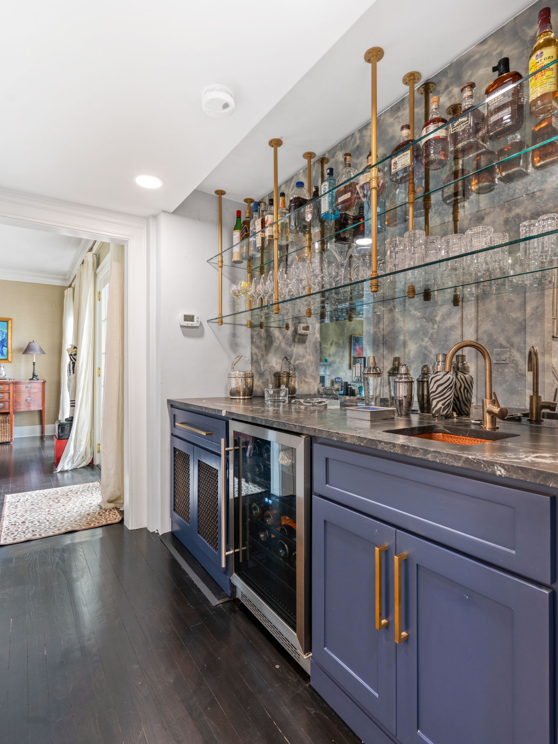 Bar with blue cabinets, wine fridge, liquor shelves, and sink. Dark wood floor.